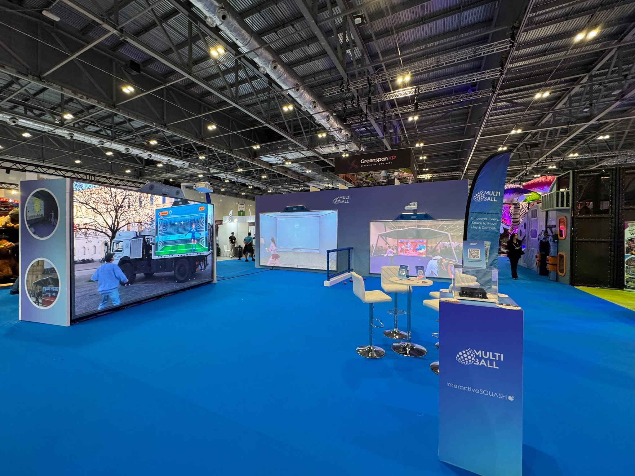 Multiball stand at IAAPA Expo Europe 2026 showing the back-wall projection screens, net divider and branded PC plinth