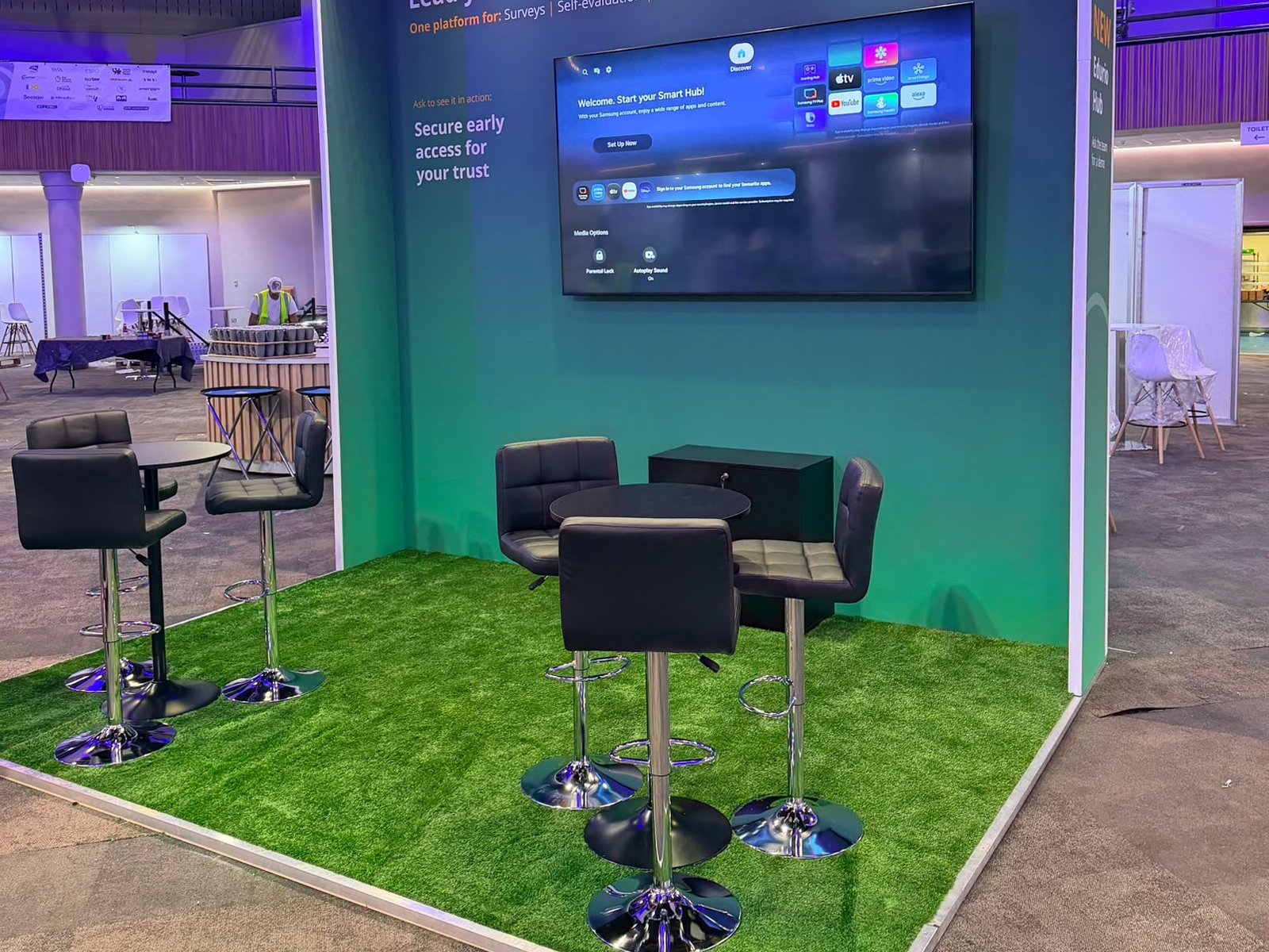 Open corner of the Edurio stand with artificial grass platform floor, aluminium edging, high tables and stools