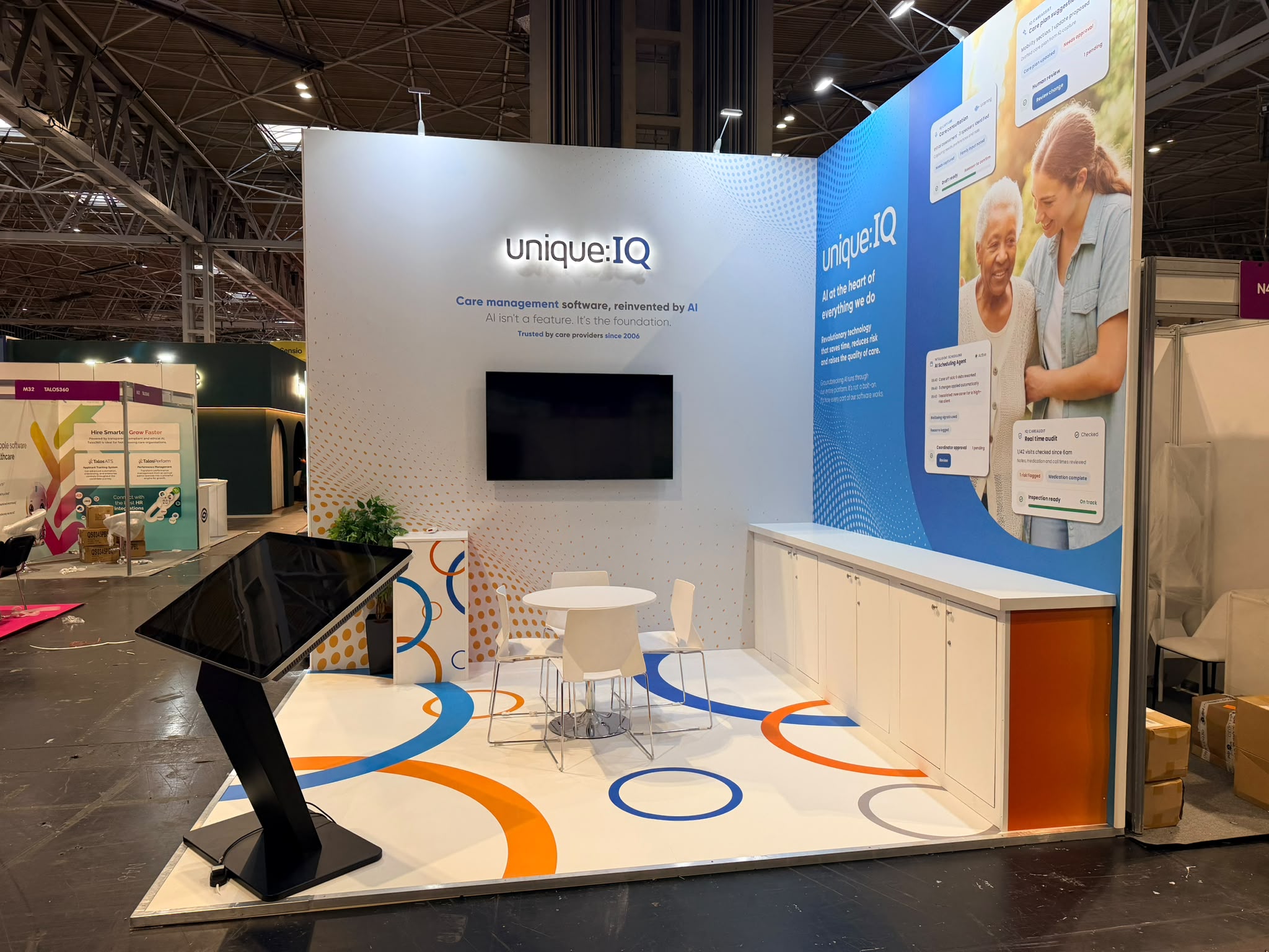 Unique IQ stand showing the printed vinyl floor with blue and orange circle motif, freestanding touchscreen totem and meeting table